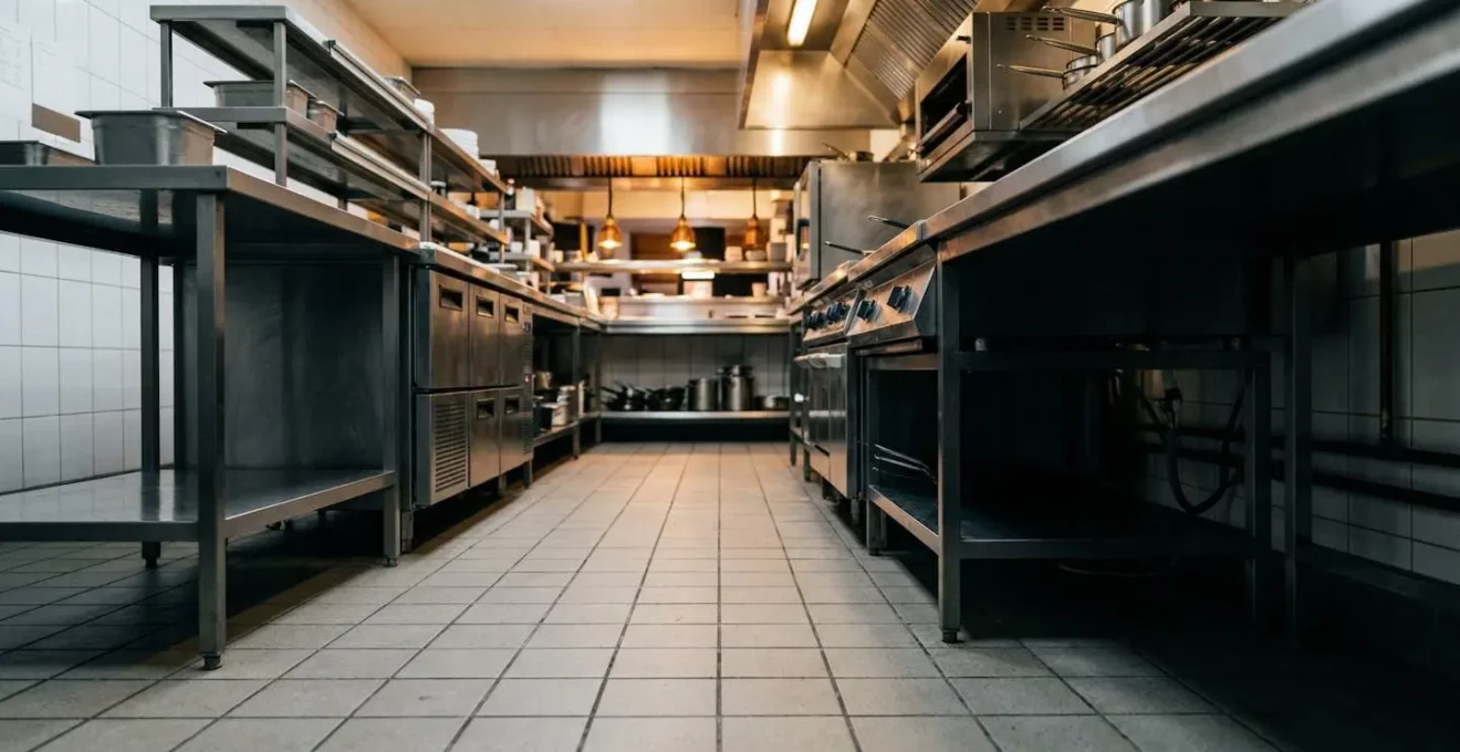 Vue macro d'une cuisine professionnelle de restaurant avec détails de surfaces métalliques et zones d'ombre propices aux nuisibles